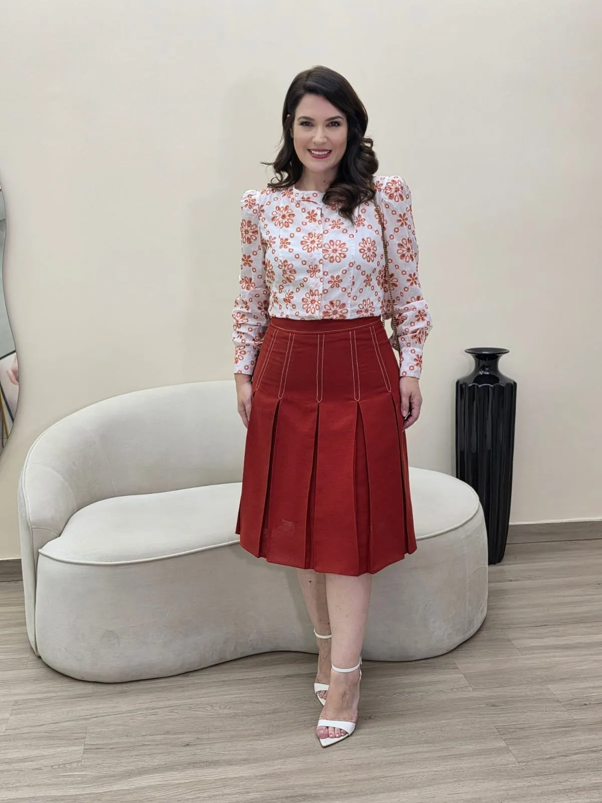 Modelo veste blusa branca com flores em terracota e saia de pregas terracota abaixo do joelho