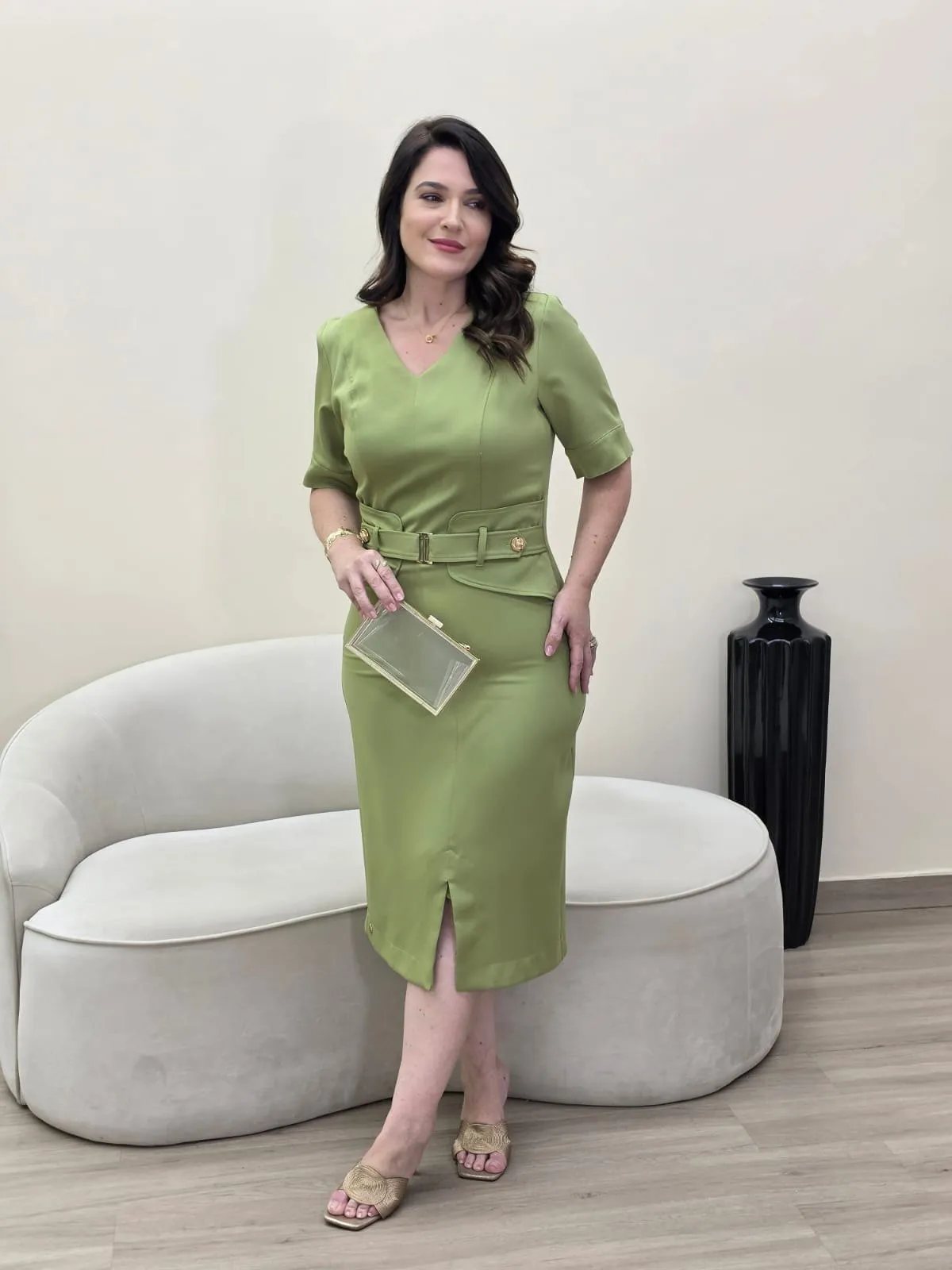 Modelo veste conjunto verde-alface de blusa com decote em V e cinto, e saia lápis com fenda à frente