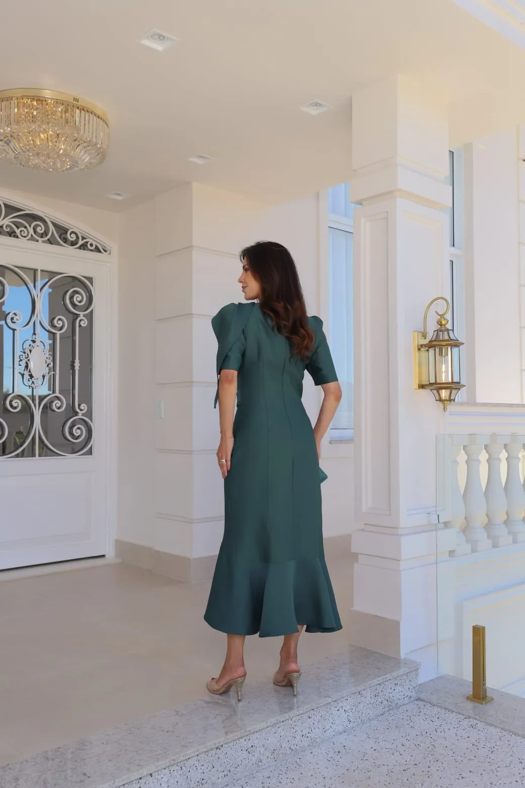 Modelo veste conjunto verde-esmeralda de blusa com laço no ombro e saia sereia com folho na barra