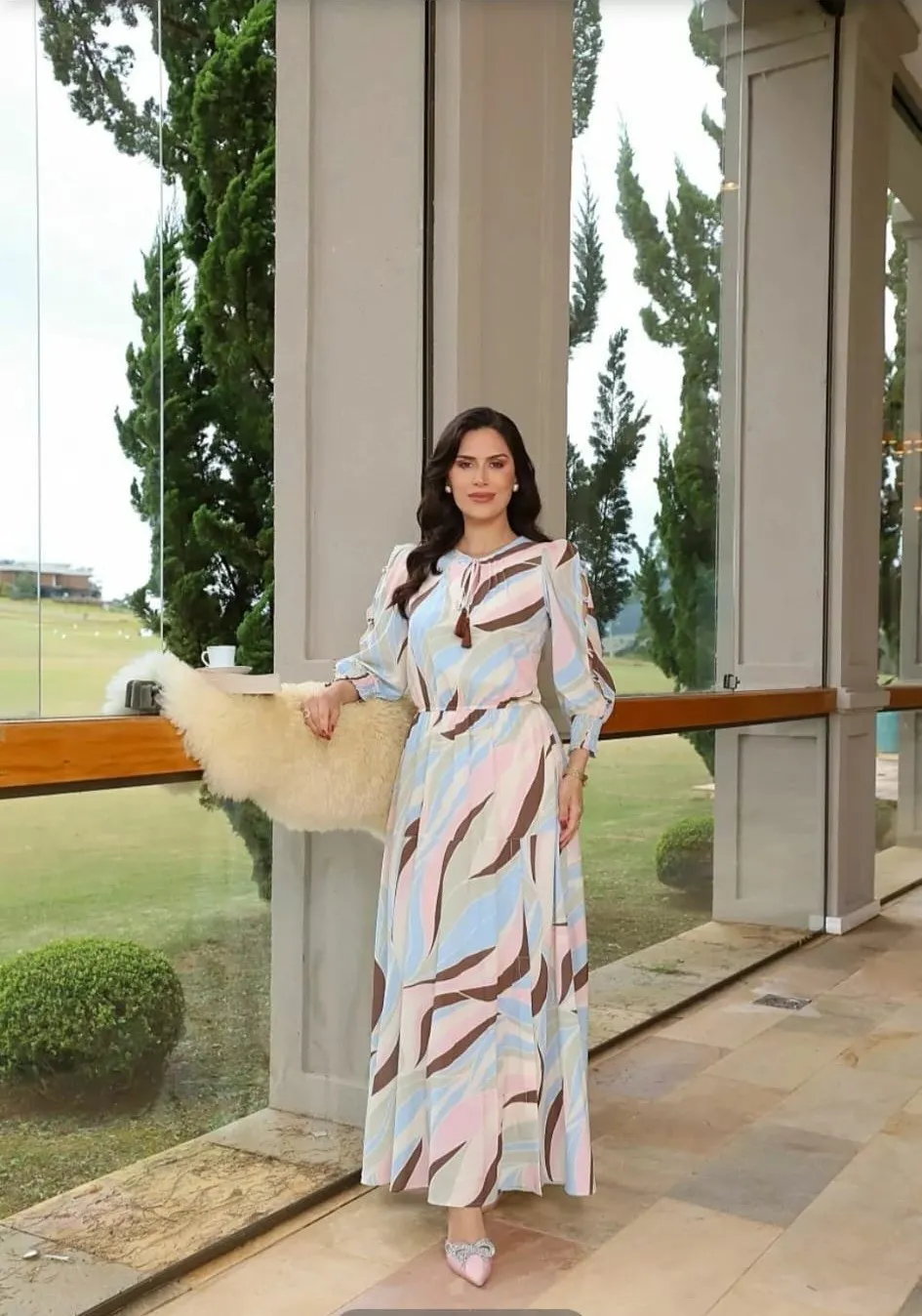 Modelo veste vestido comprido com estampado ondulado em tons de rosa, azul e castanho, com laço no decote