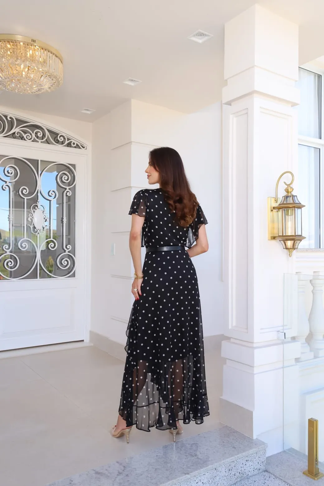 Vestido comprido preto com poá branco, decote em V, mangas curtas soltas e barra assimétrica
